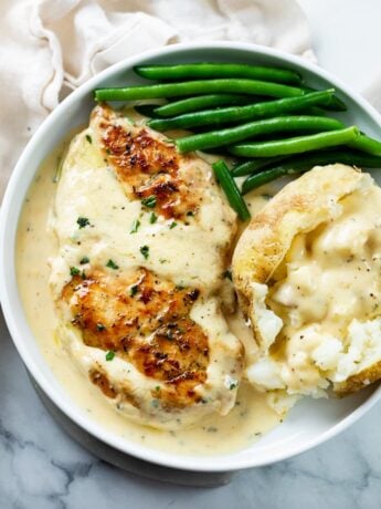 A white plate with Creamy Ranch Chicken next to a baked potato and green beans.