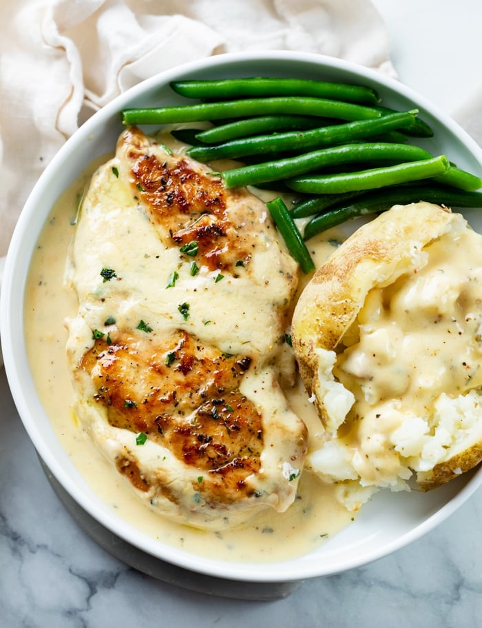 A white plate with Ranch Chicken on top next to green beans and a baked potato.