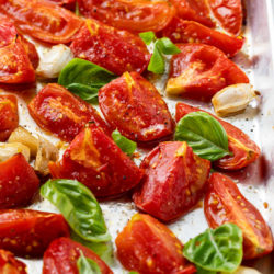Roasted tomatoes on a light baking sheet with basil.
