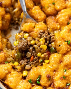 A spoon scooping up tater tot casserole with ground beef, corn, and crispy tater tots.