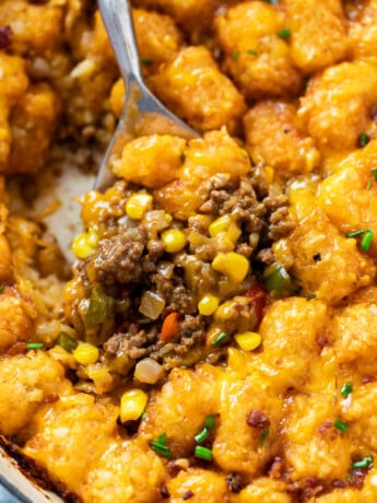 A spoon scooping up tater tot casserole with ground beef, corn, and crispy tater tots.