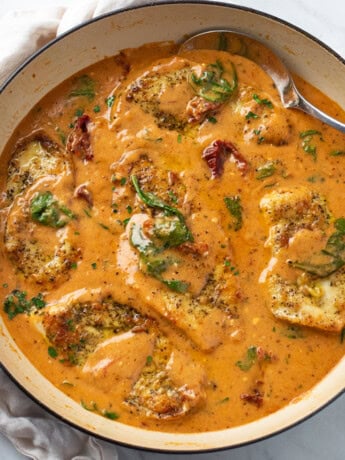 A skillet filled with Tuscan Chicken in sauce with sundried tomatoes and spinach.