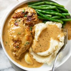 A white plate with Creamy Garlic Chicken next to mashed potatoes and green beans.