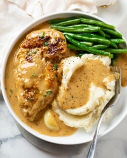 A white plate with Creamy Garlic Chicken next to mashed potatoes and green beans.