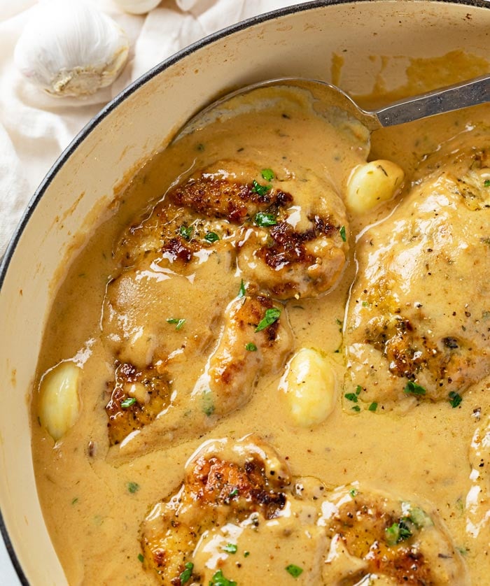 Creamy Garlic Chicken in a skillet with garlic and a spoon with lots of gravy.