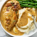 A white Plate with creamy garlic chicken next to mashed potatoes and green beans.