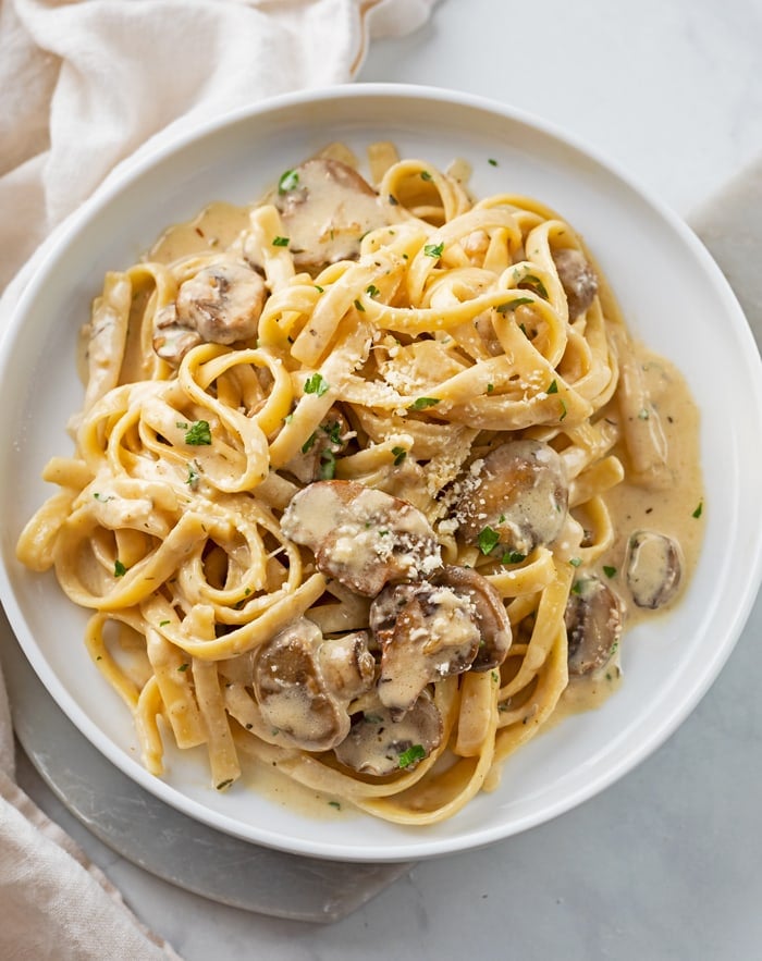 A white plate topped with Creamy Mushroom Pasta with Fettuccine noodles and parsley.