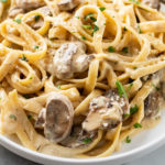 Creamy mushroom pasta on a white plate topped with fresh parsley.