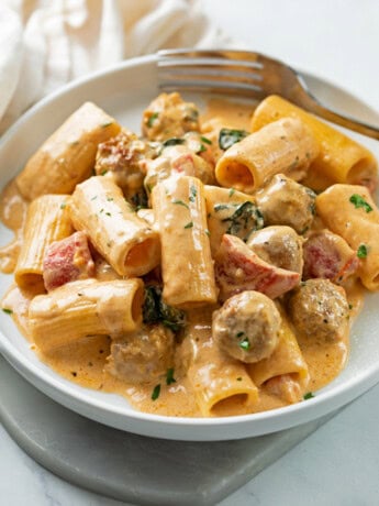 A white plate with creamy sausage pasta with roasted red peppers and rigatoni.