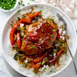 A white plate Honey Garlic Chicken on top of rice with Broccoli and Red Peppers.