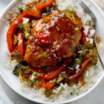 A white plate with Honey Garlic Chicken on top of rice with red bell peppers and broccoli.