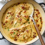A skillet with Creamy Bacon Chicken topped with crispy bacon in a creamy sauce.