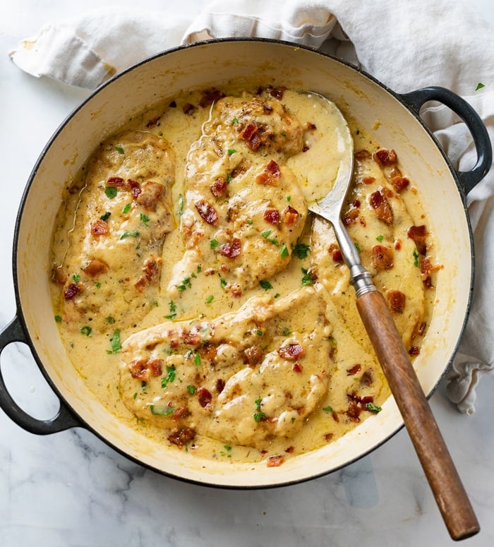 A skillet filled with Chicken in a creamy sauce topped with crispy bacon.