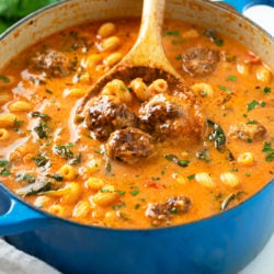 A blue dutch oven filled with Meatball Soup with meatballs, pasta, spinach, and parsley.