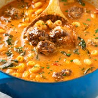 A wooden spoon scooping up Meatball soup with meatballs and noodles in a tomato based broth.