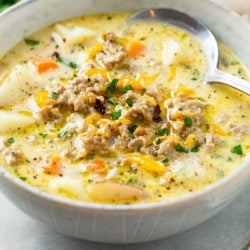 A bowl of creamy sausage potato soup topped with melted cheese.