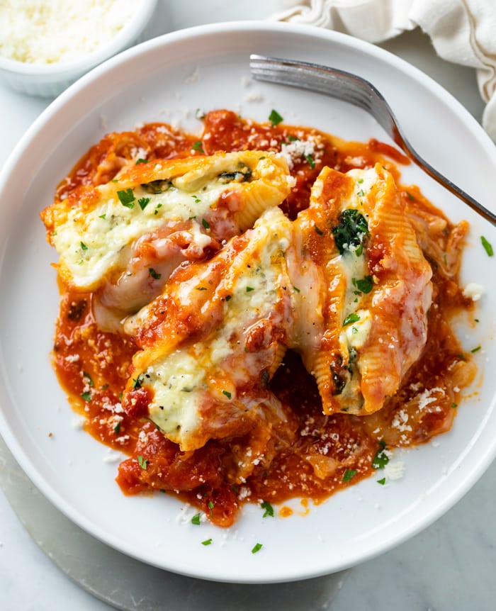 A white plate with cheesy Stuffed Shells on top with a fork.