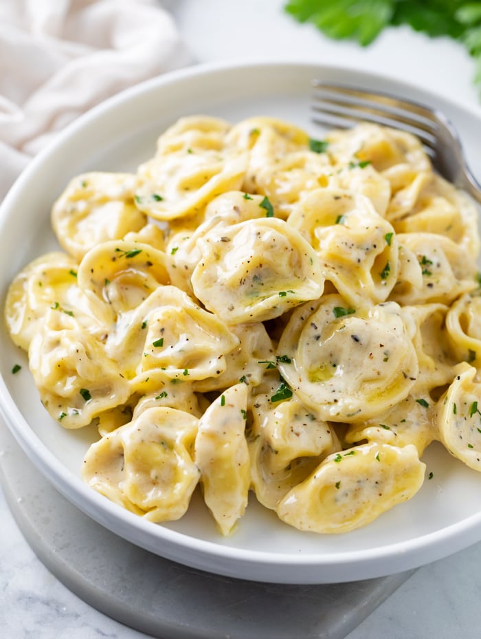 A white plate with tortellini in a cream sauce with herbs.