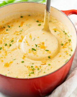 A ladle scooping up Cheesy Potato Soup from a red Dutch oven.