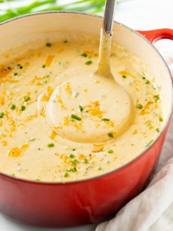 A ladle scooping up Cheesy Potato Soup from a red Dutch oven.