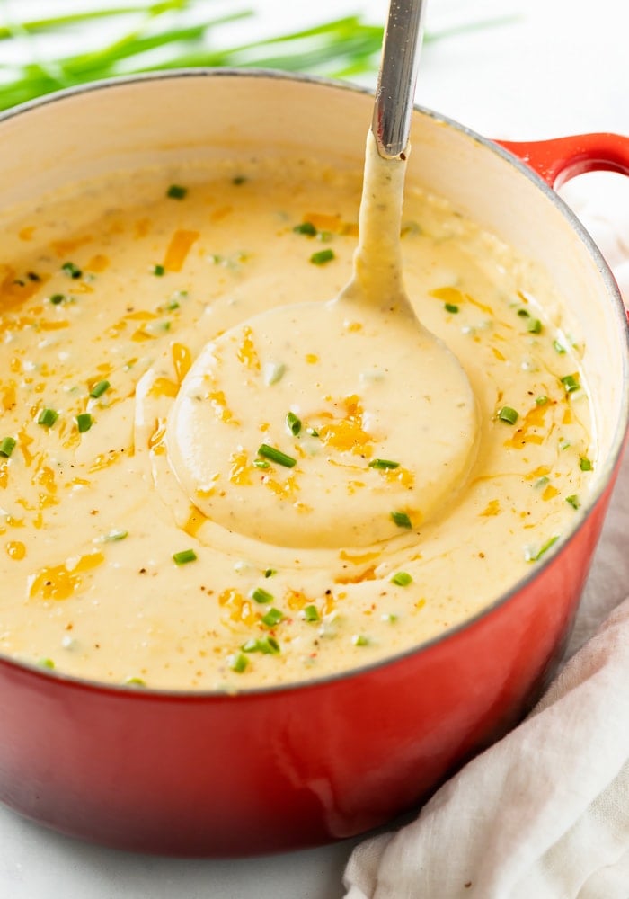 A ladle scooping up Cheesy Potato Soup from a red Dutch oven.