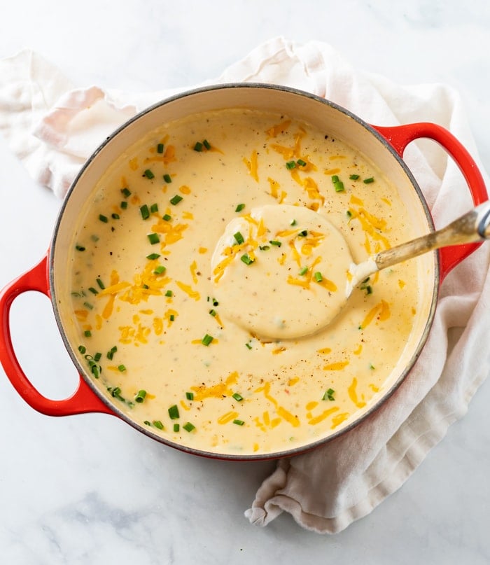 A red Dutch oven filled with Cheesy Potato Soup topped with cheese and chives.