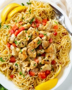 A white platter with Chicken Scampi topped with diced tomatoes, parsley, and slices of lemon.