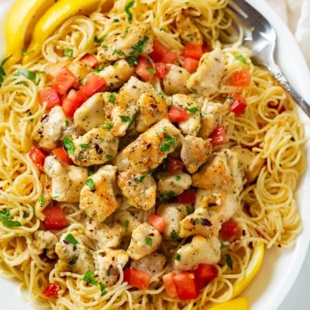 A white platter with Chicken Scampi topped with diced tomatoes, parsley, and slices of lemon.