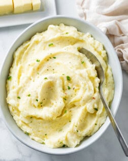 A white bowl of creamy homemade mashed potatoes with a spoon in it.