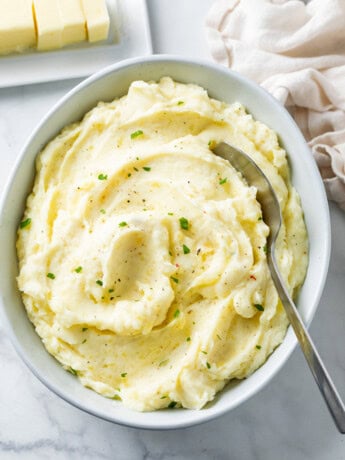 A white bowl of creamy homemade mashed potatoes with a spoon in it.