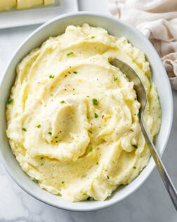 A white bowl of creamy homemade mashed potatoes with a spoon in it.