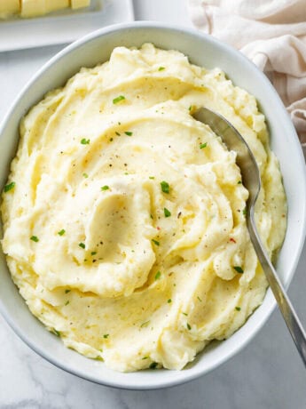 A white bowl of creamy homemade mashed potatoes with a spoon in it.