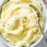 A white bowl with creamy mashed potatoes with a spoon in it.