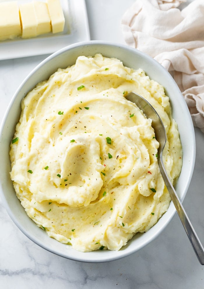 A white bowl of creamy homemade mashed potatoes with a spoon in it.