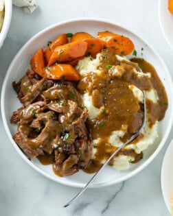 Mississippi Pot Roast on a white plate with carrots, mashed potatoes, and gravy.