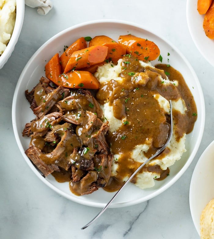 Mississippi Pot Roast on a white plate with carrots, mashed potatoes, and gravy.