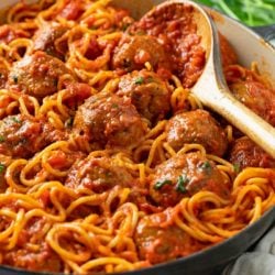 A pot of Spaghetti and Meatballs with a wooden spoon on the side and parsley in the background.