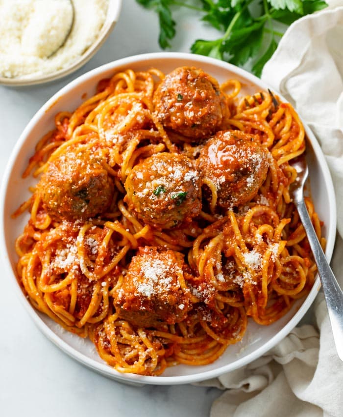 A white plate with Spaghetti and Meatballs topped with Parmesan cheese and a fork on the side.