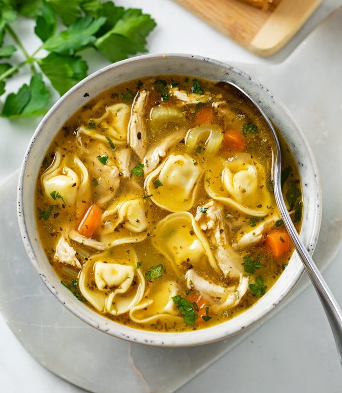 A bowl filled with Chicken Tortellini Soup with a spoon in it.