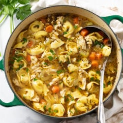 Chicken Tortellini Soup in a green soup pot with a ladle on the side.