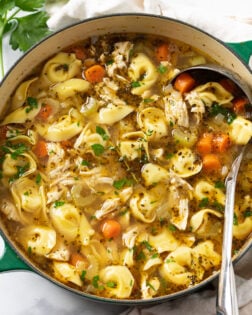 Chicken Tortellini Soup in a green soup pot with a ladle on the side.