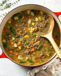 A red Dutch oven filled with Hamburger Soup with a wooden spoon.