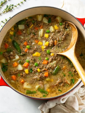 A red Dutch oven filled with Hamburger Soup with a wooden spoon.