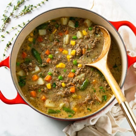 A red Dutch oven filled with Hamburger Soup with a wooden spoon.