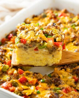 A wooden spatula holding up a slice of Hashbrown Breakfast Casserole with sausage, peppers, and cheese.