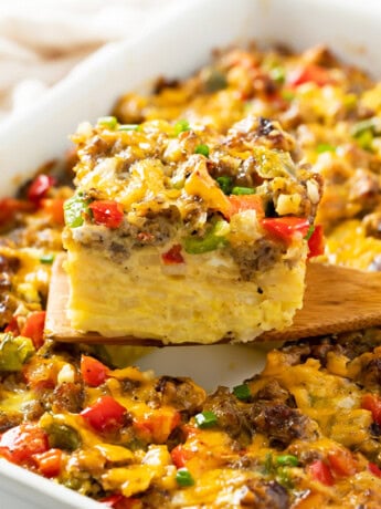 A wooden spatula holding up a slice of Hashbrown Breakfast Casserole with sausage, peppers, and cheese.