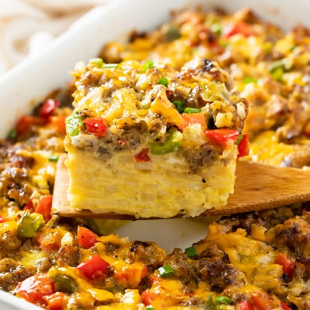 A wooden spatula holding up a slice of Hashbrown Breakfast Casserole with sausage, peppers, and cheese.