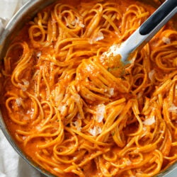 Roasted Red Pepper Pasta in a skillet with kitchen tongs scooping it up.