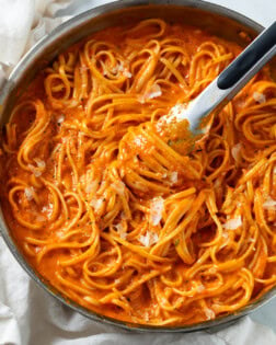 Roasted Red Pepper Pasta in a skillet with kitchen tongs scooping it up.