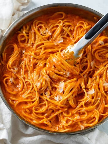 Roasted Red Pepper Pasta in a skillet with kitchen tongs scooping it up.